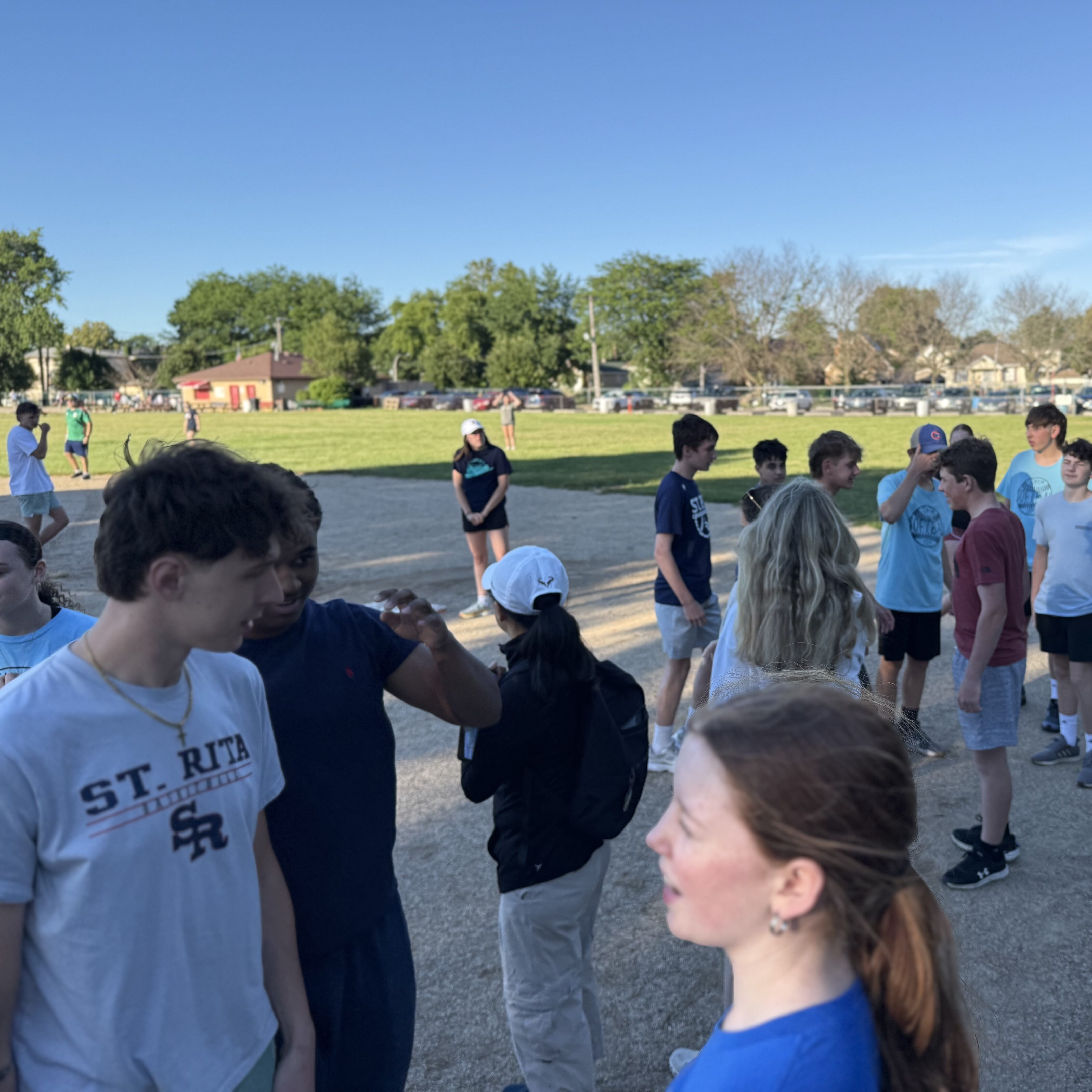 Group of youth stand around talking on a baseball pitch.