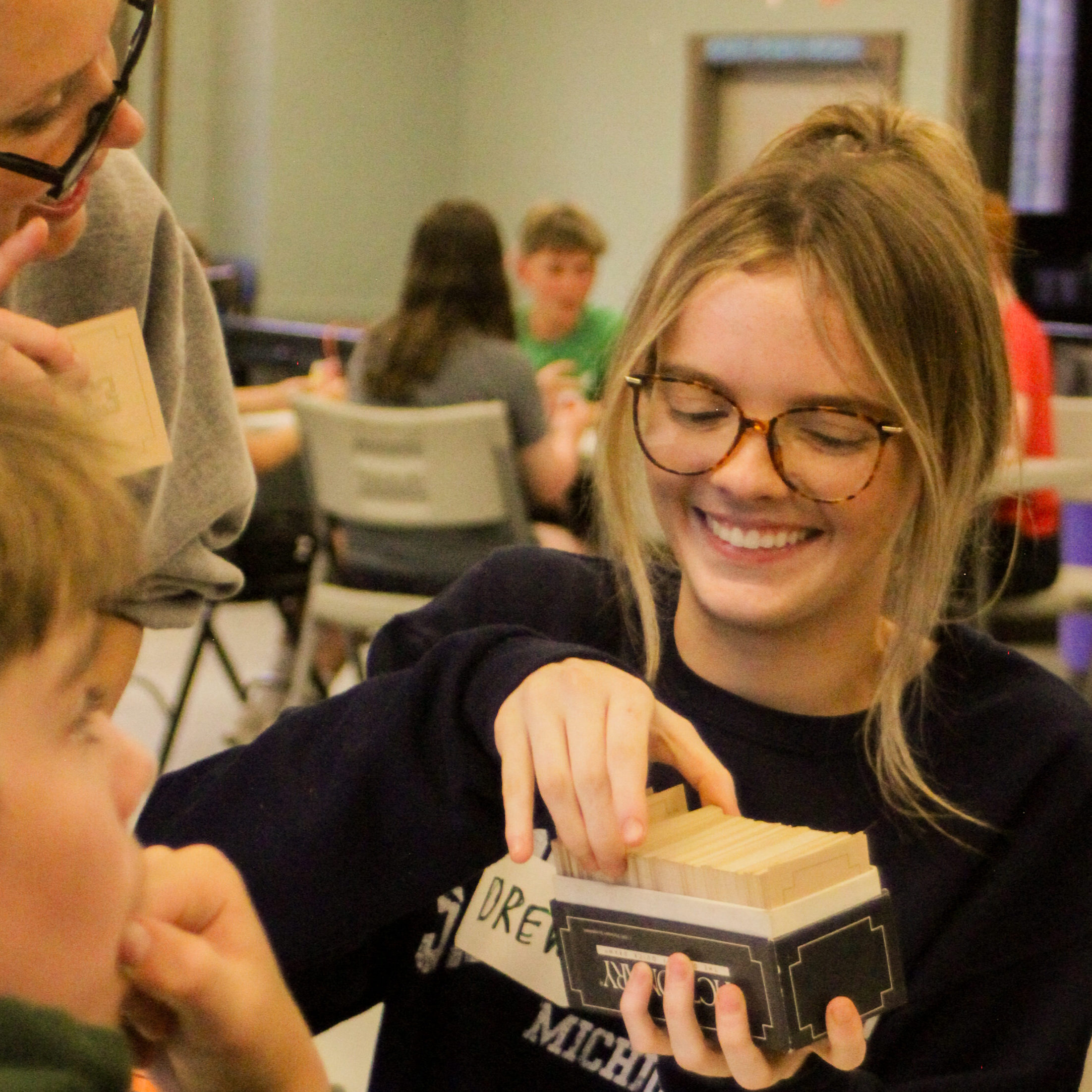 Young person smiles while drawing a card out of a trivia box