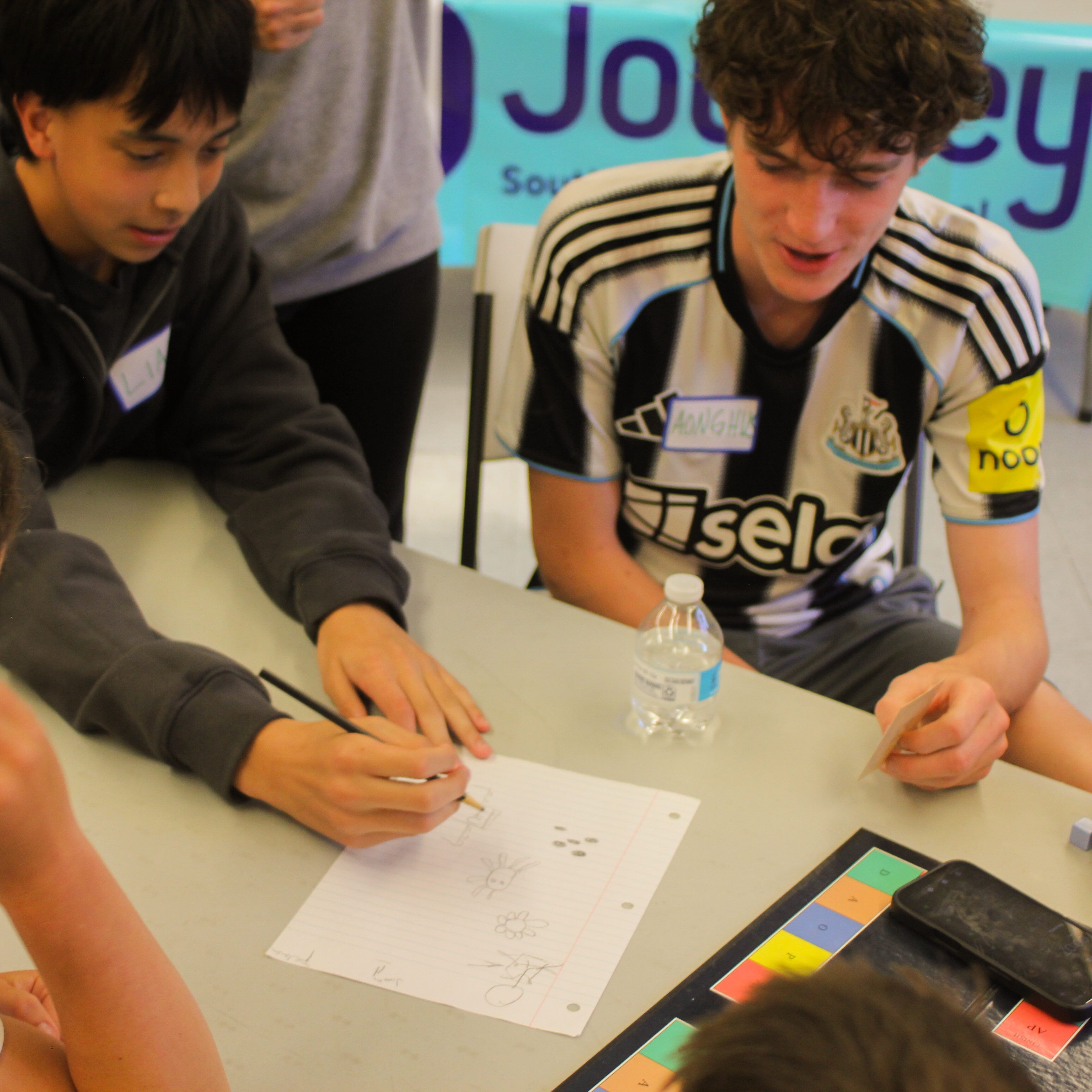 Two young people smile at table with pen, paper and gameboard